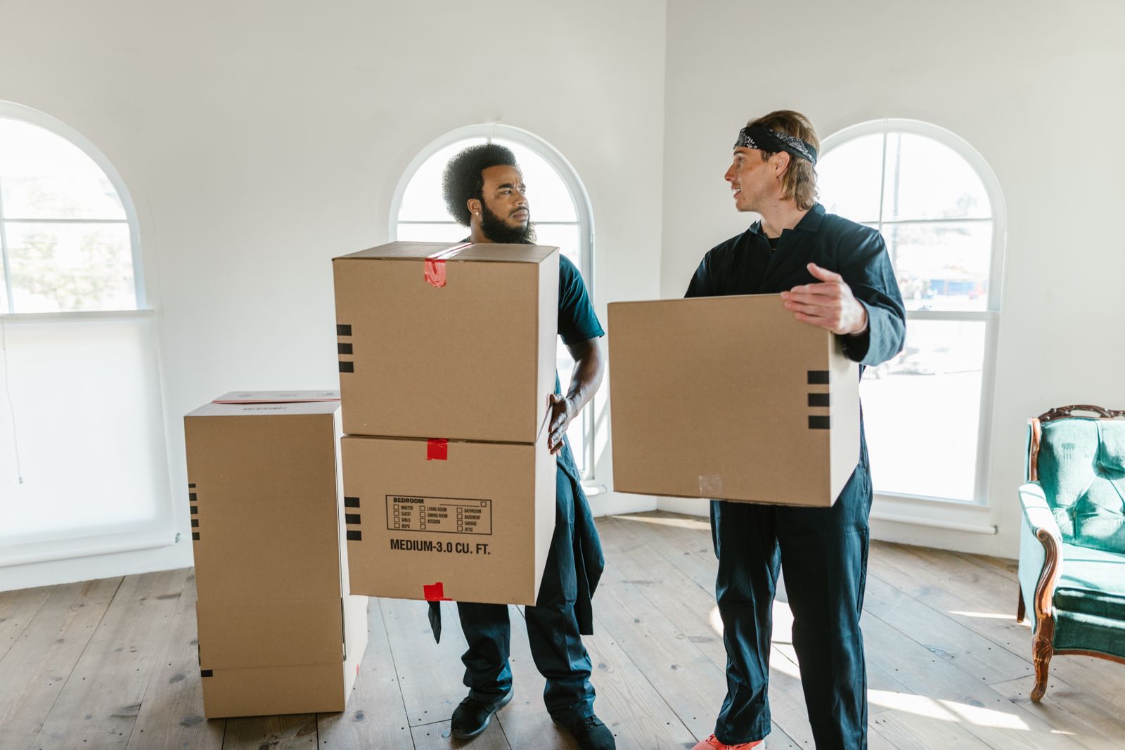 Two removalists carrying moving boxes through a bright room